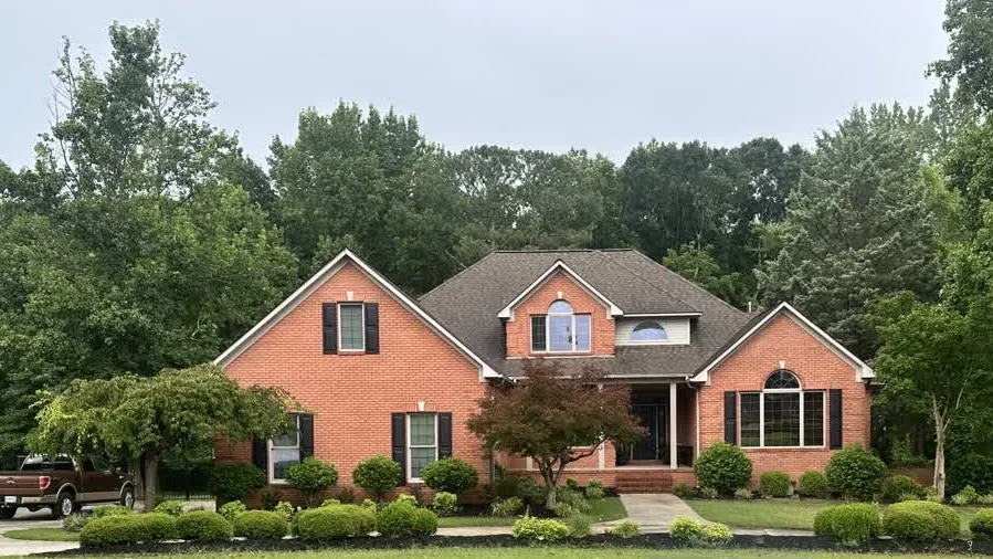 Red brick two-story home with a shingle roof surrounded by mature trees in Middle Tennessee