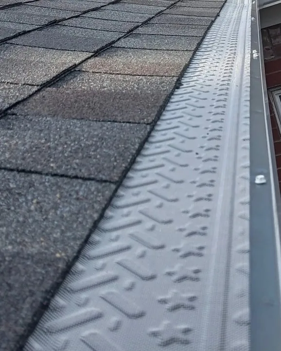 Embossed micro-mesh gutter guard fastened to a gutter beneath architectural shingles