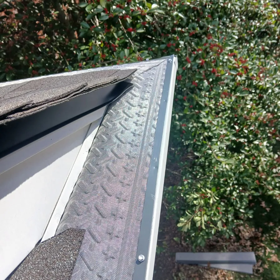 Gutter guard mitered around a roof corner and fastened to the gutter lip above a hedge
