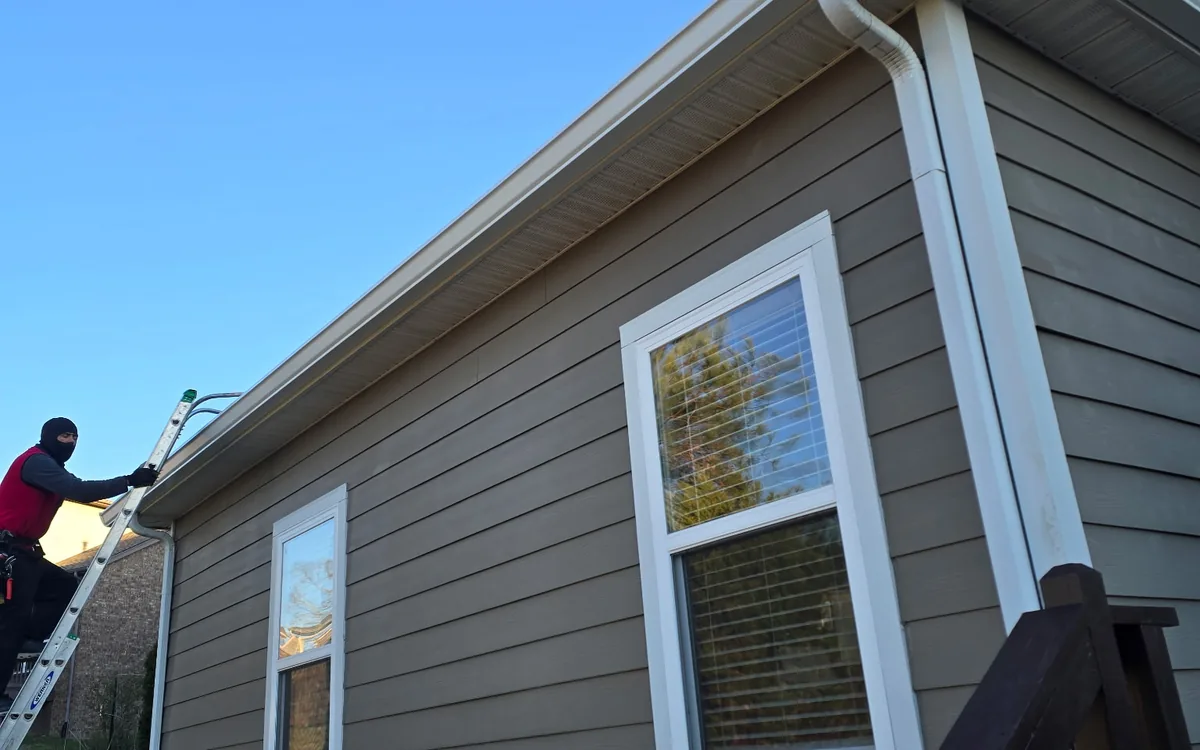 Lap siding home with white seamless gutters and downspouts while a crew member works from a ladder