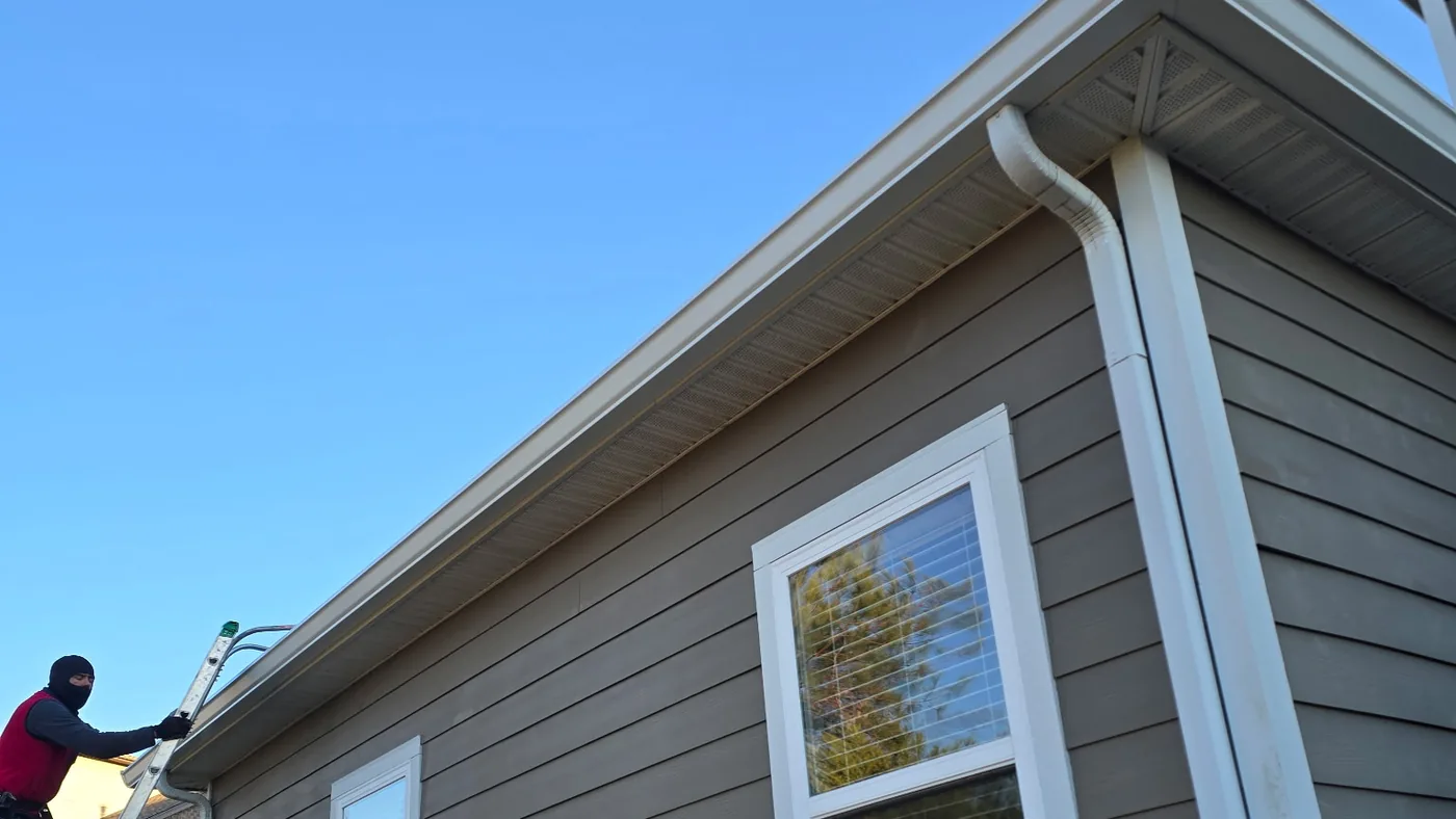 Lap siding home with white seamless gutters and downspouts while a crew member works from a ladder