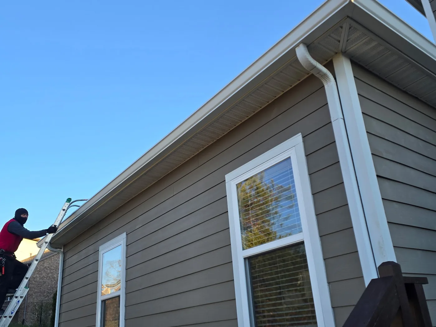 Lap siding home with white seamless gutters and downspouts while a crew member works from a ladder