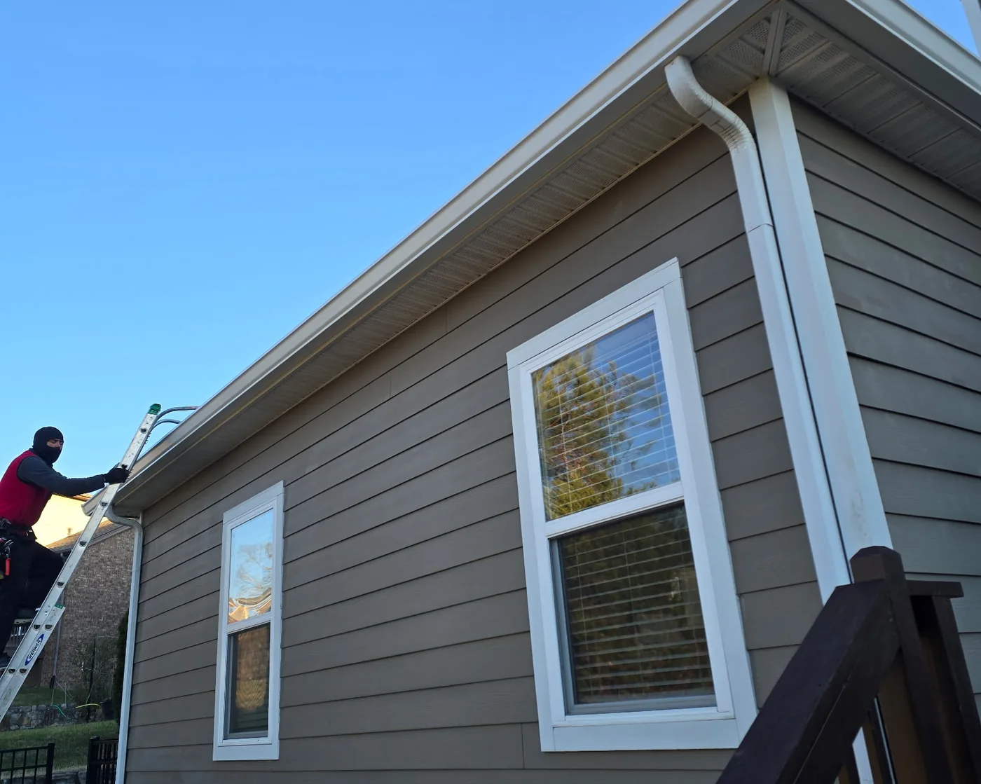 Lap siding home with white seamless gutters and downspouts while a crew member works from a ladder