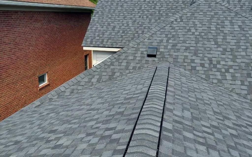 Newly installed gray architectural shingle roof with ridge vent on a brick home