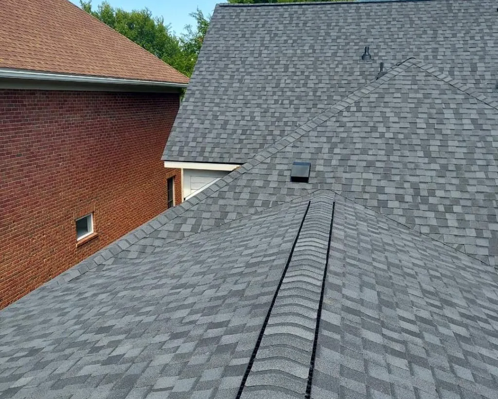 Newly installed gray architectural shingle roof with ridge vent on a brick home